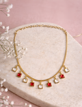 Gold necklace with red and clear square pendants on a pink background