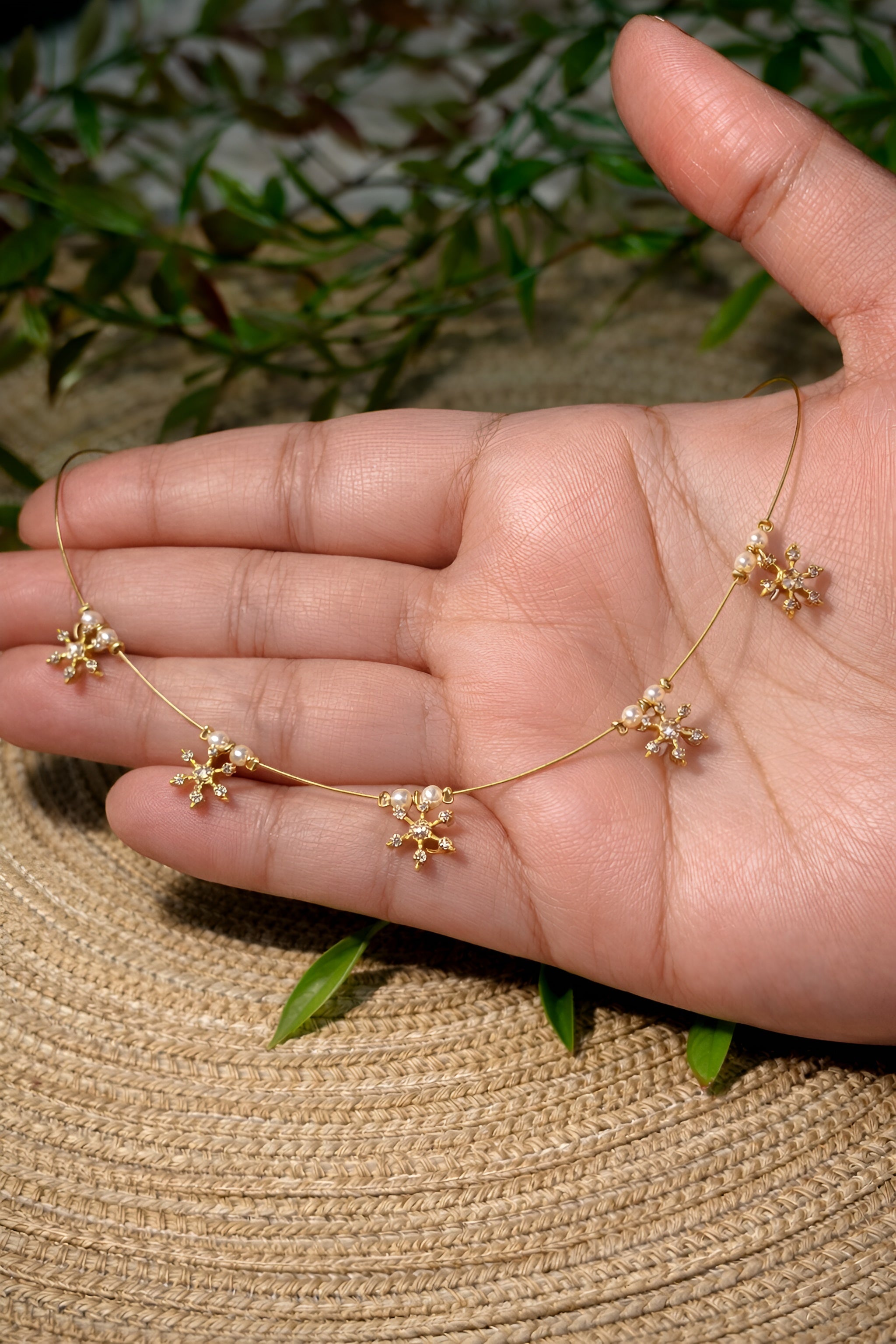 Gold necklace with floral pendants held in a hand against a natural background