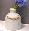 White vase with gold necklace and blue tulips on a gray background